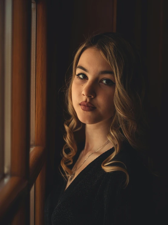 a beautiful woman in black dress posing by a window