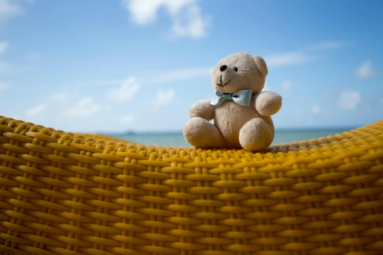 a stuffed teddy bear sits in a yellow chair at the beach