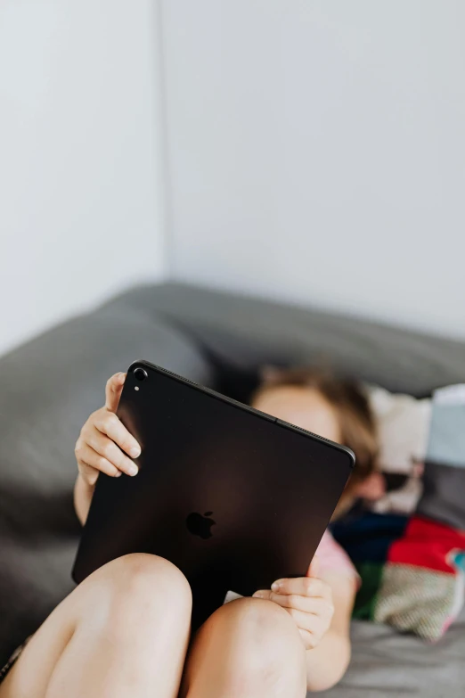 a girl using an ipad while laying on a bed