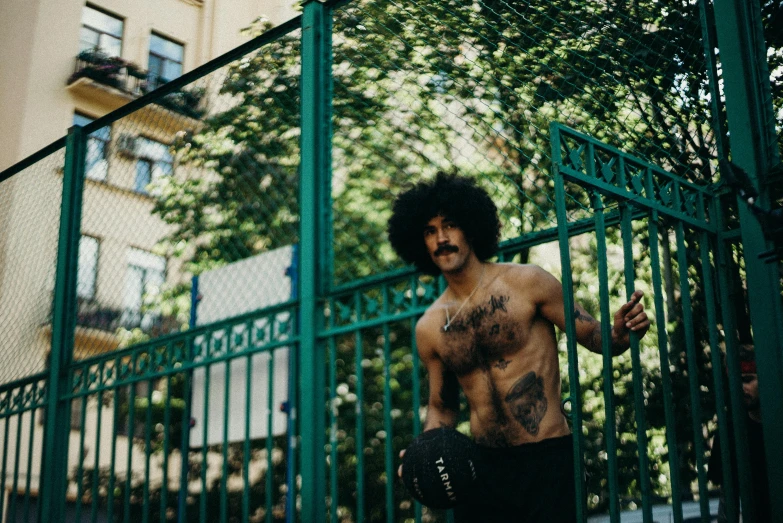 a shirtless man leans against a fence and walks