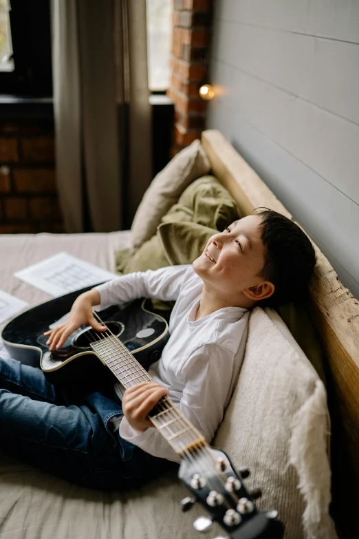 a woman holding an acoustic guitar while sitting on a bed
