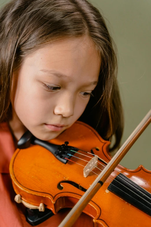 a little girl playing a violin while wearing an orange outfit