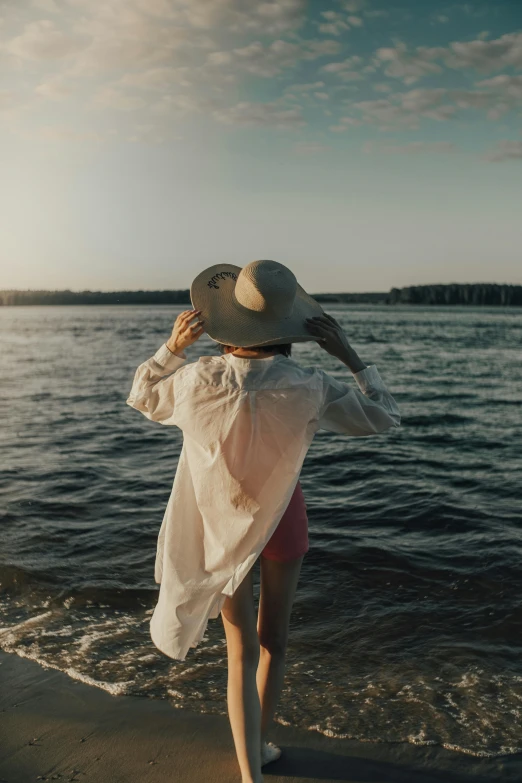 a woman in a hat is walking near the water