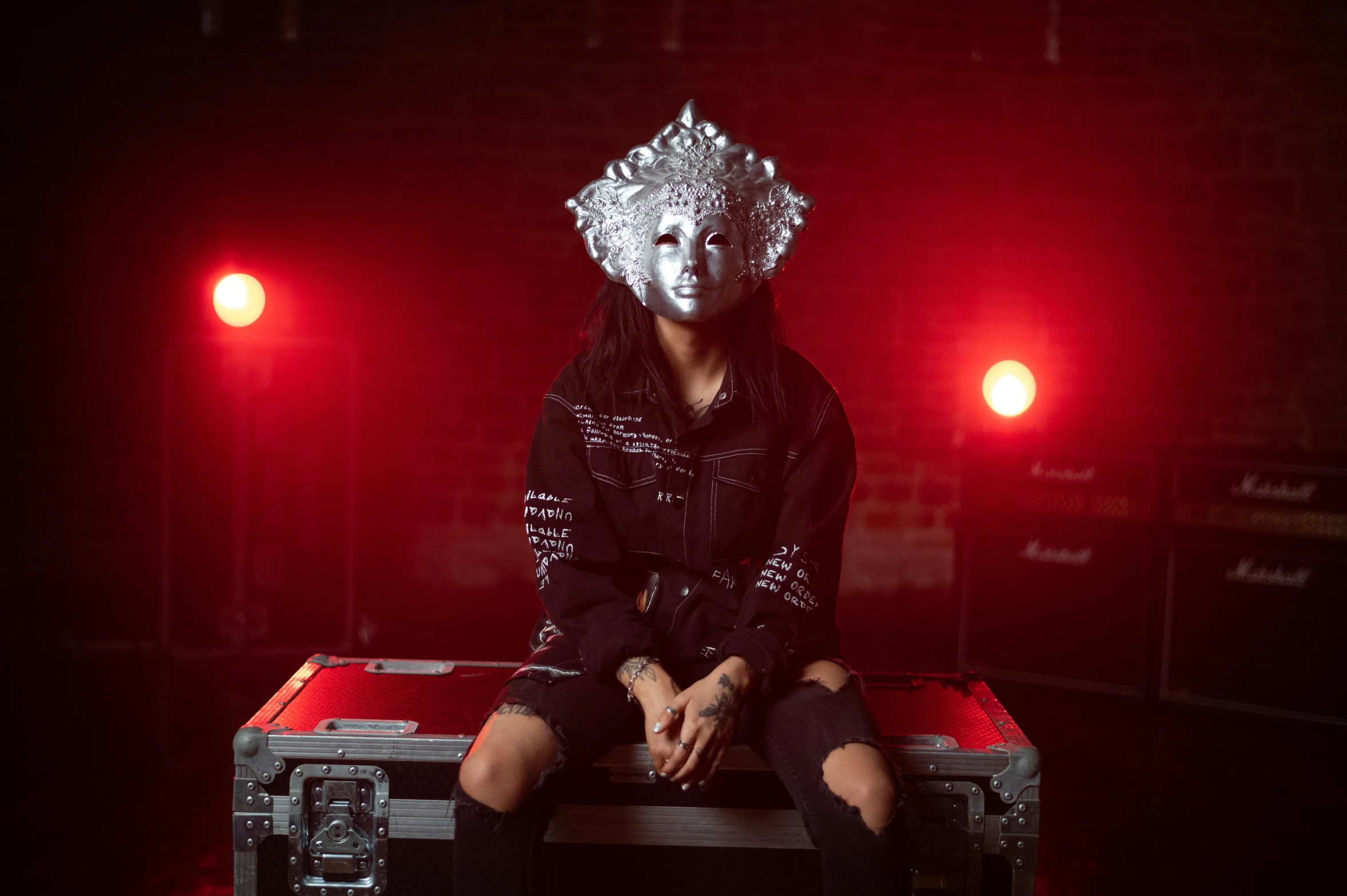 woman with a silver hairdo sits on a metal toolbox in front of red light