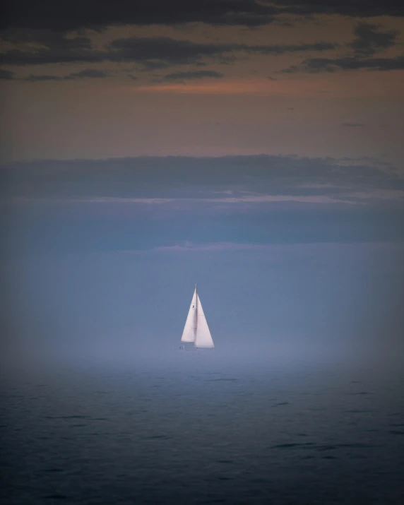 a lone sailboat in the water on a foggy day