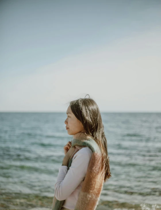 a girl is standing on the beach and looking out to sea