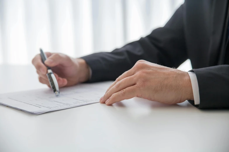 person in suit holding pens writing on document