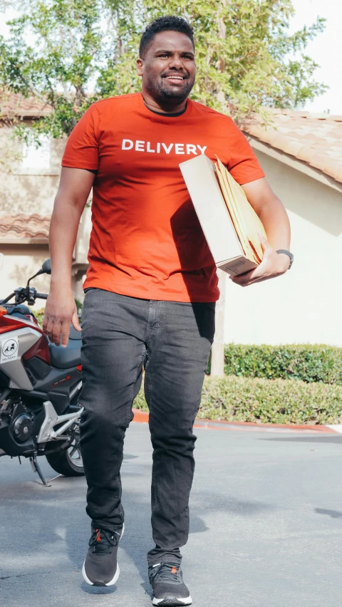 a black man in an orange shirt is holding a pizza