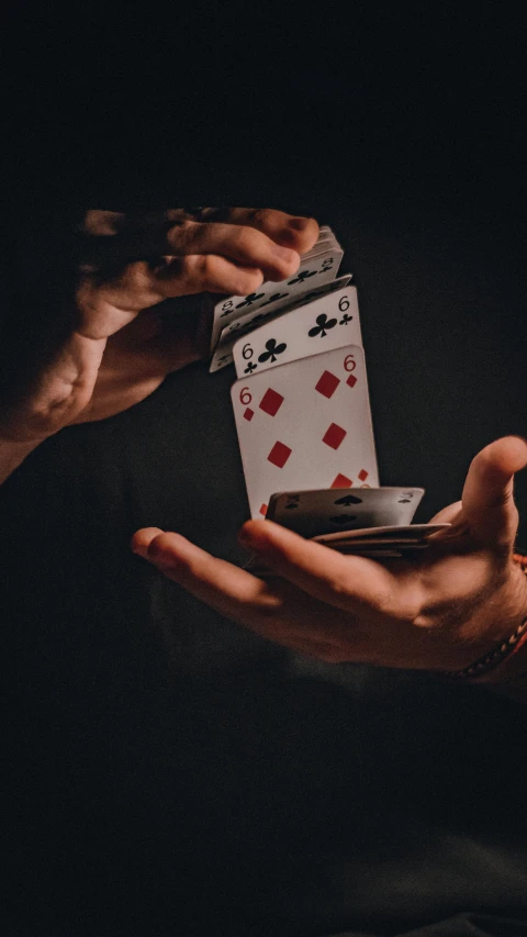 two hands are holding playing cards and an electronic device