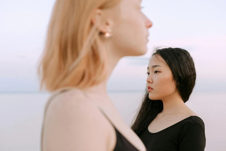 two woman are staring at the ocean near each other