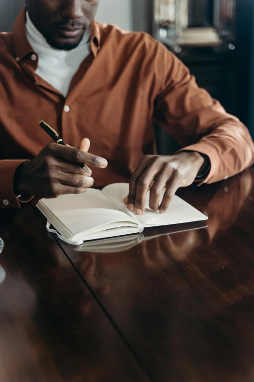 man writing in notepad on wooden table