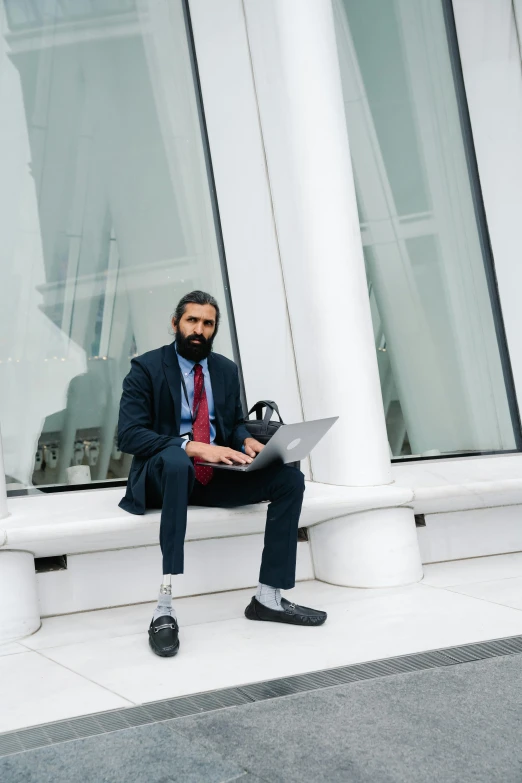 a man in a business suit sits on a bench outside a building