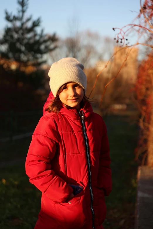 a young woman in a red jacket with a white hat standing outdoors