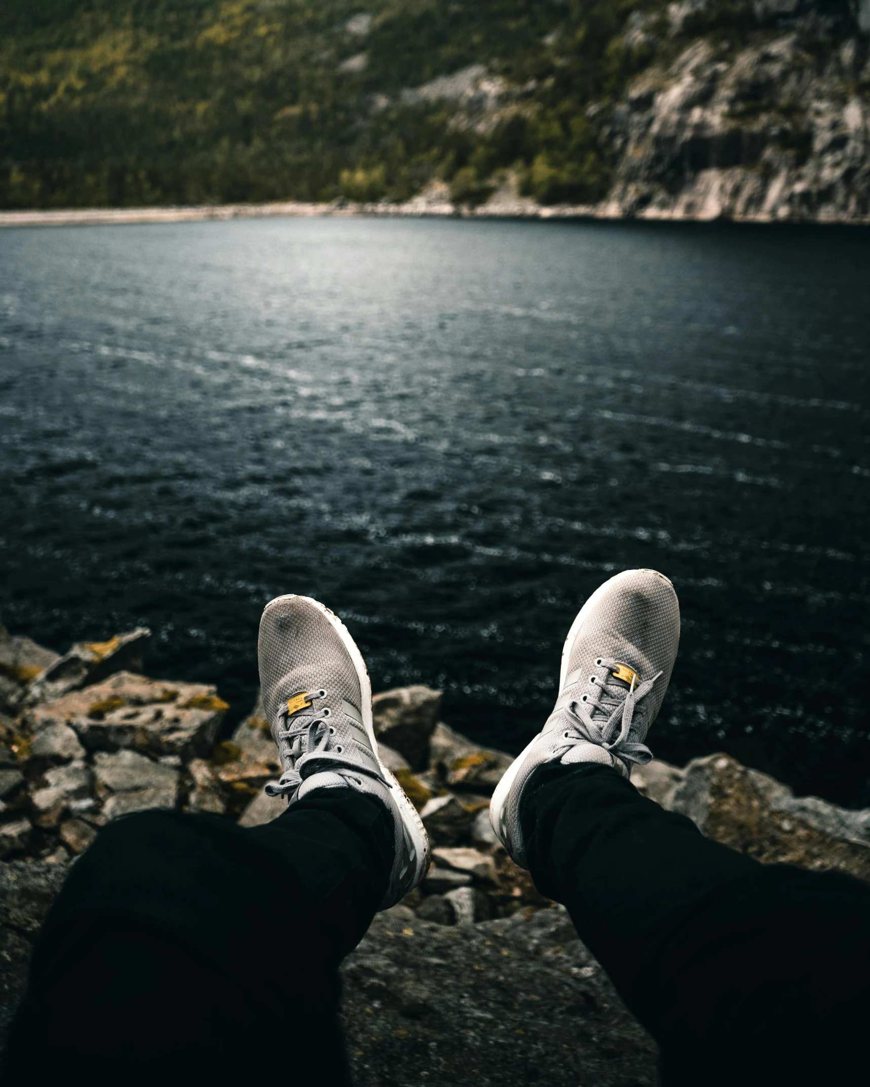 someone wearing running shoes on rocks by the water