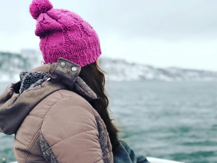 a woman in a pink beanie standing at the side of a body of water