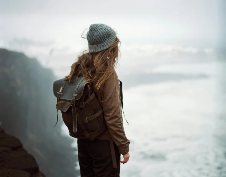 a woman in a hat and coat standing on top of a cliff