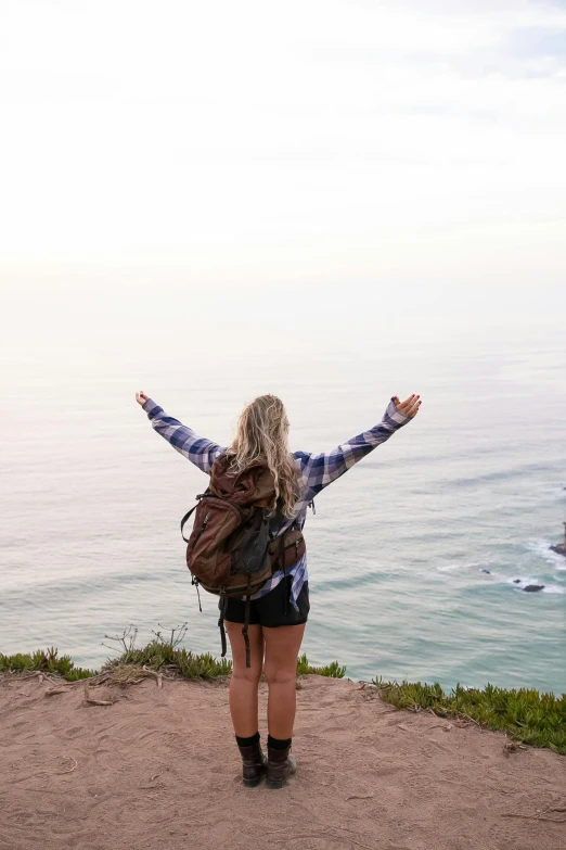 a girl with her arms outstretched is standing on a cliff overlooking a body of water