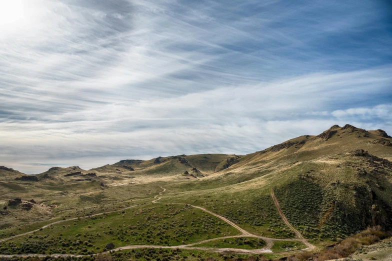 a road in the middle of a mountain under a cloudy blue sky