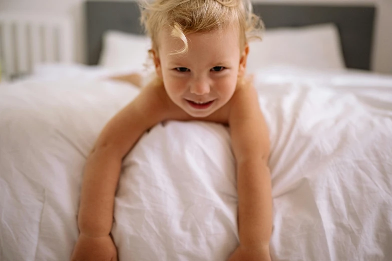 a child laying on top of a bed with white sheets