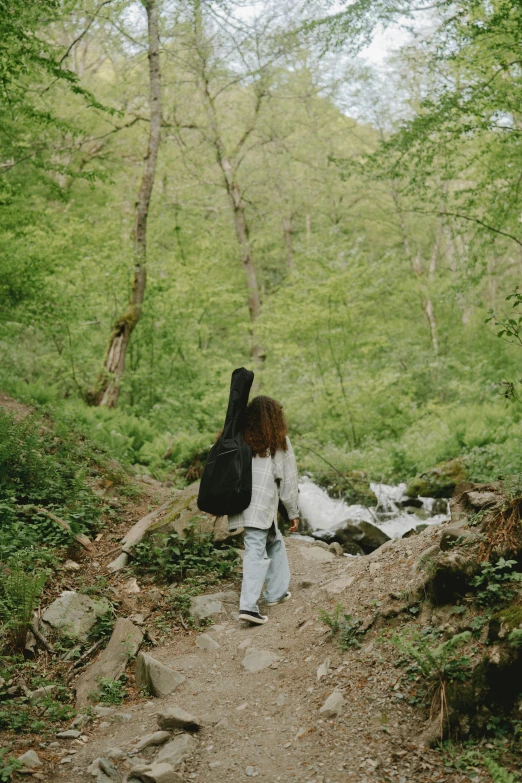 a woman carrying a black backpack is walking down a trail