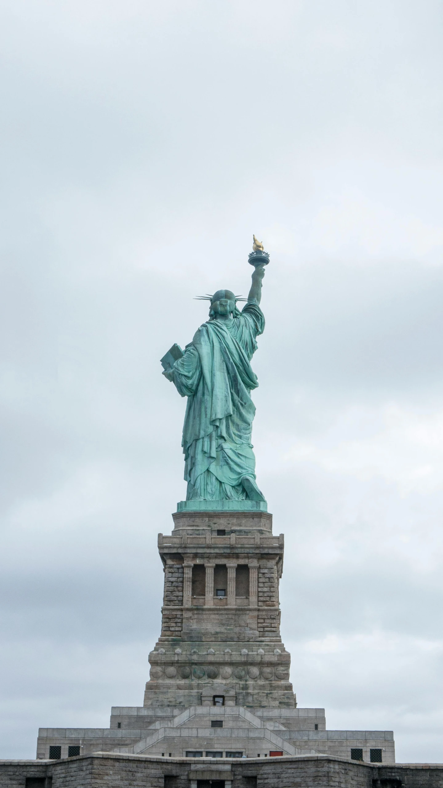 the statue of liberty stands in the foreground and clouds loom above it