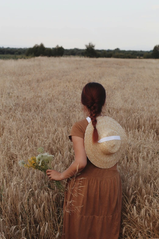 a woman walking through a tall field holding a flower