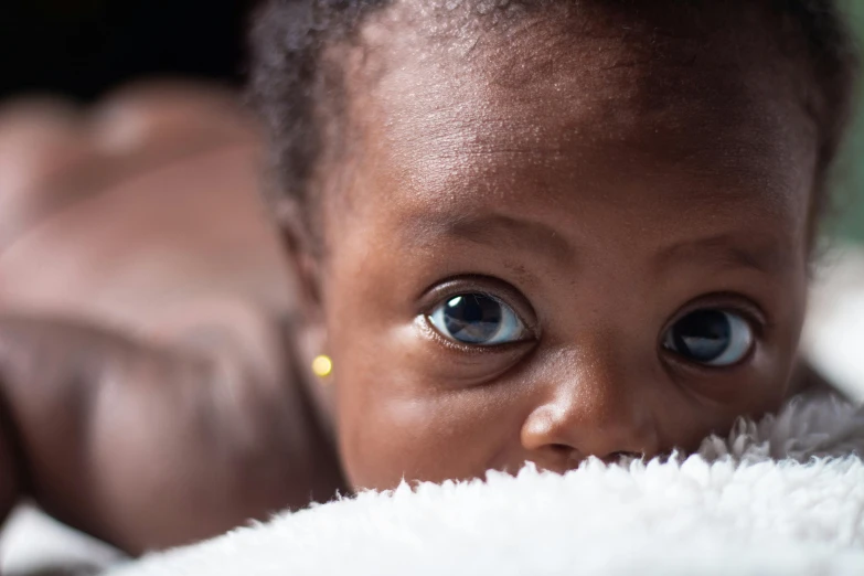 baby with big eyes laying on blanket staring at camera