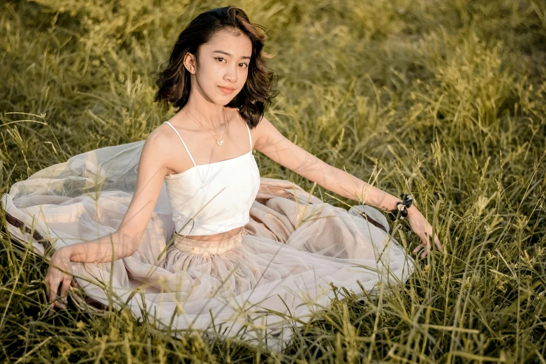a woman sitting in the tall grass wearing a white tank top