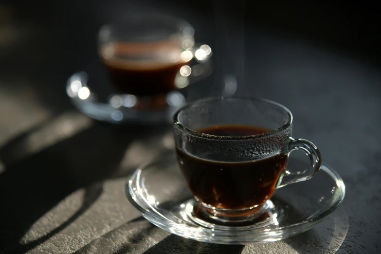 two tea cups, one with dark coffee on a table