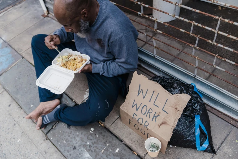 a homeless man eats some food off of his lunch box