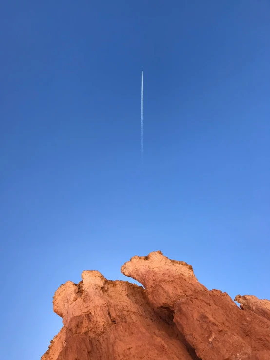 a jet flying through a blue sky next to rocks