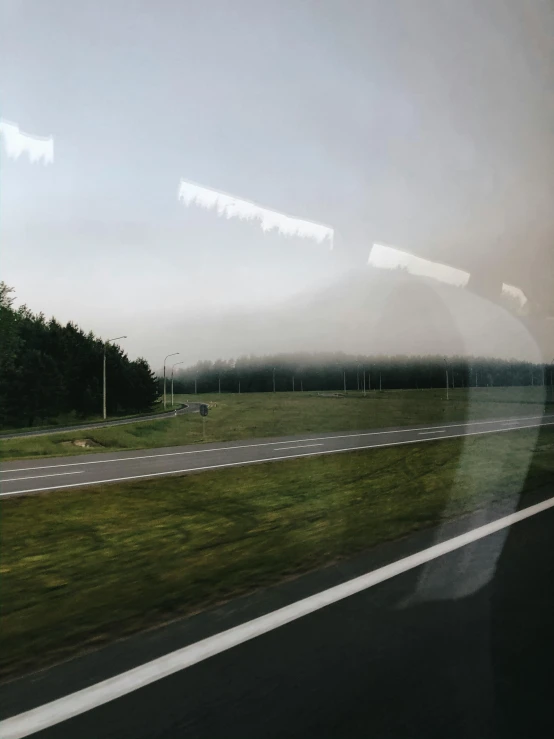 a picture out a train window showing a field near the road