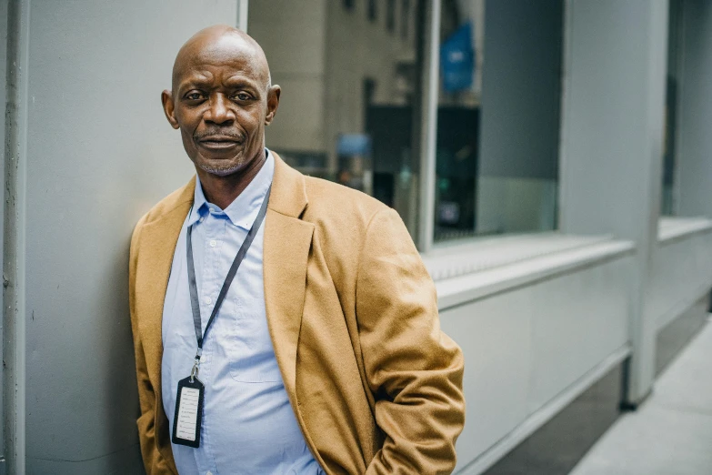 an african man wearing a yellow blazer leaning against a wall