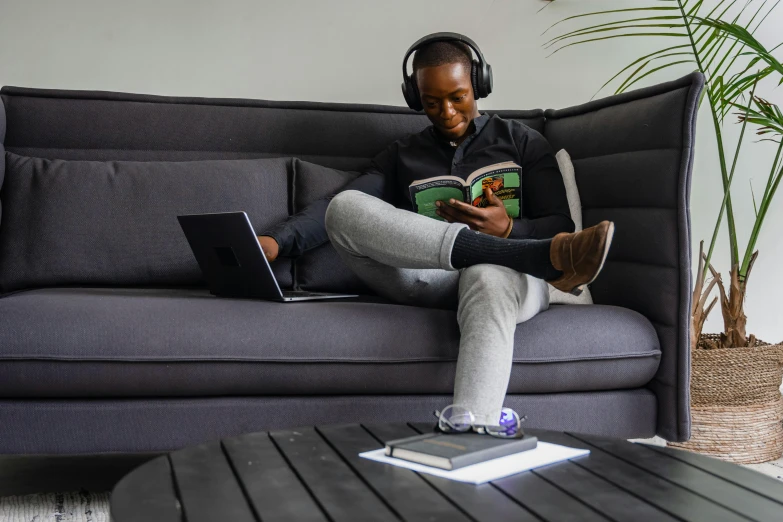 man wearing headphones sitting on a couch while looking at a book