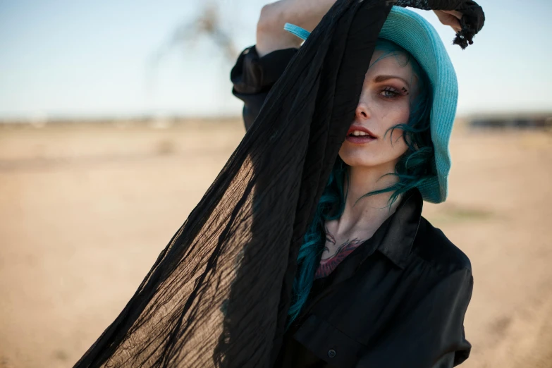 a woman wearing a turquoise hat and black dress in the desert