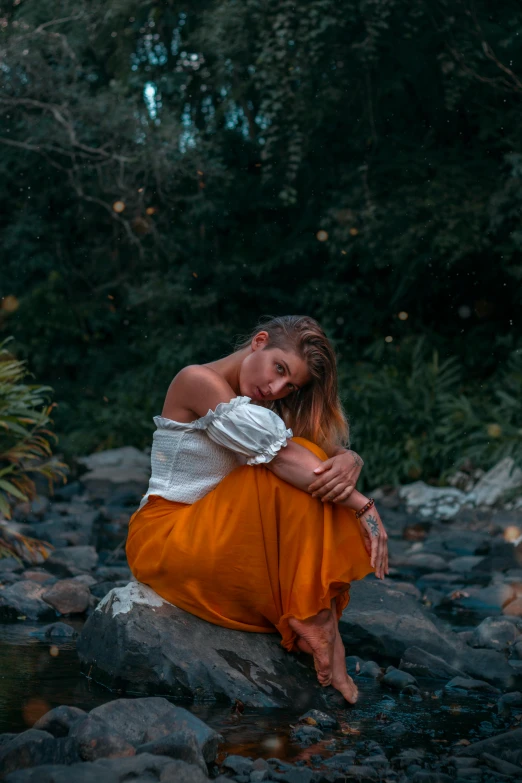 a young woman in an orange dress sitting on rocks