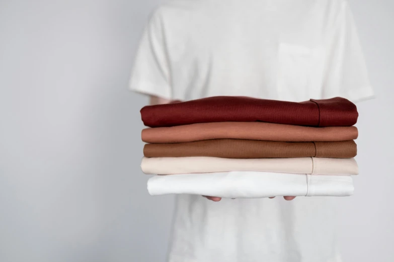 a person's hands hold stack of folded white, brown and dark colored clothing