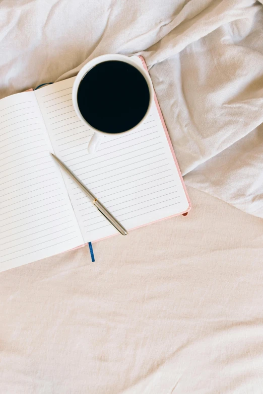 a cup of coffee and pen sitting on top of an open notebook