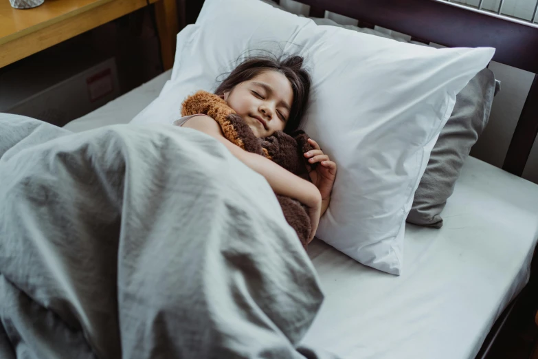 a girl laying on the bed with her teddy bear