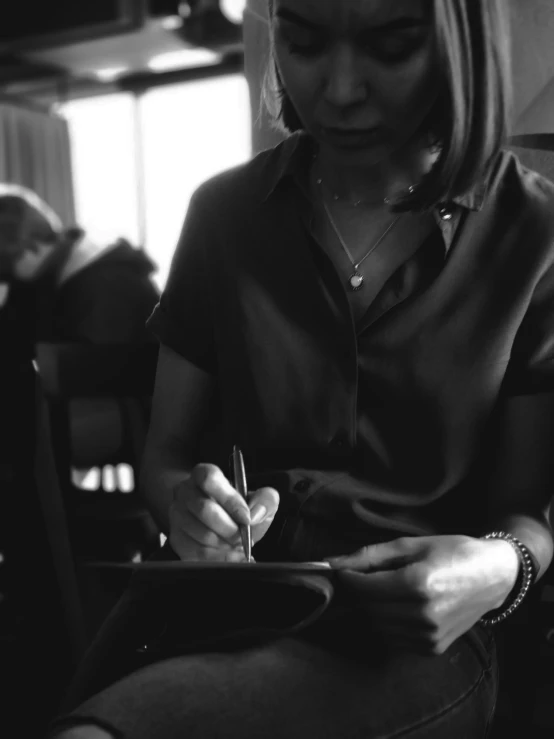 the woman is sitting in front of a laptop computer while writing on a paper