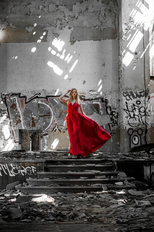 a woman in a red dress is posing near an abandoned building