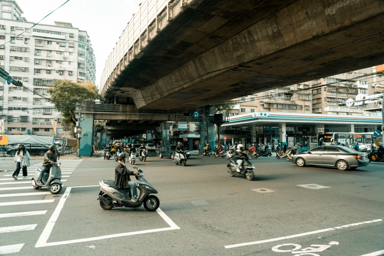 a busy intersection with multiple motor scooters riding under the overpass