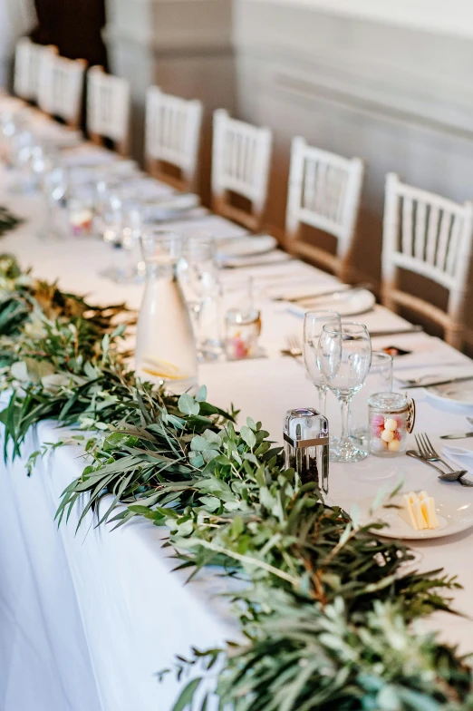 a long table decorated with place settings and eucalyptus leaves