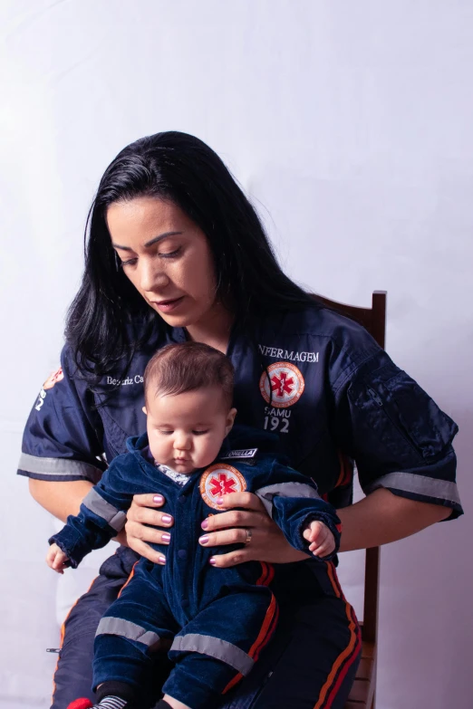 a woman in uniform holds a baby that is wearing fire gear