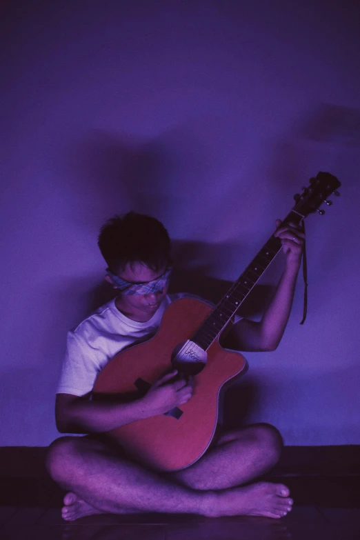 the boy is sitting down and playing his guitar