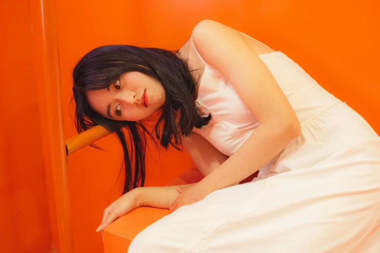a young woman leaning on a orange wall