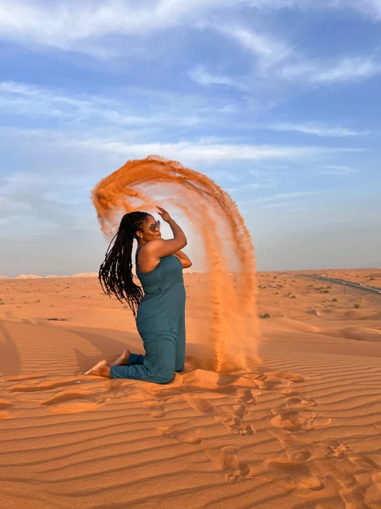 a person sitting in the middle of a desert area with sand blowing on her