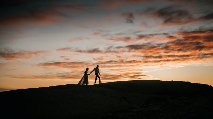 a couple of people holding hands and walking along side each other at sunset