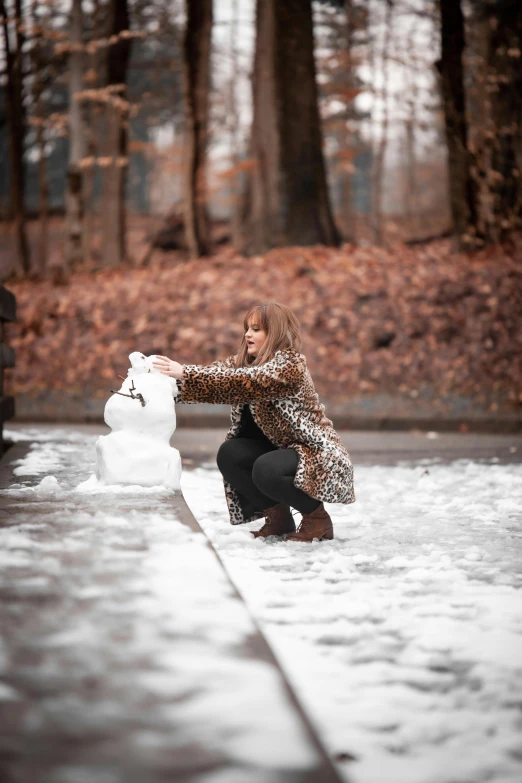 a woman kneeling down in front of a snowman