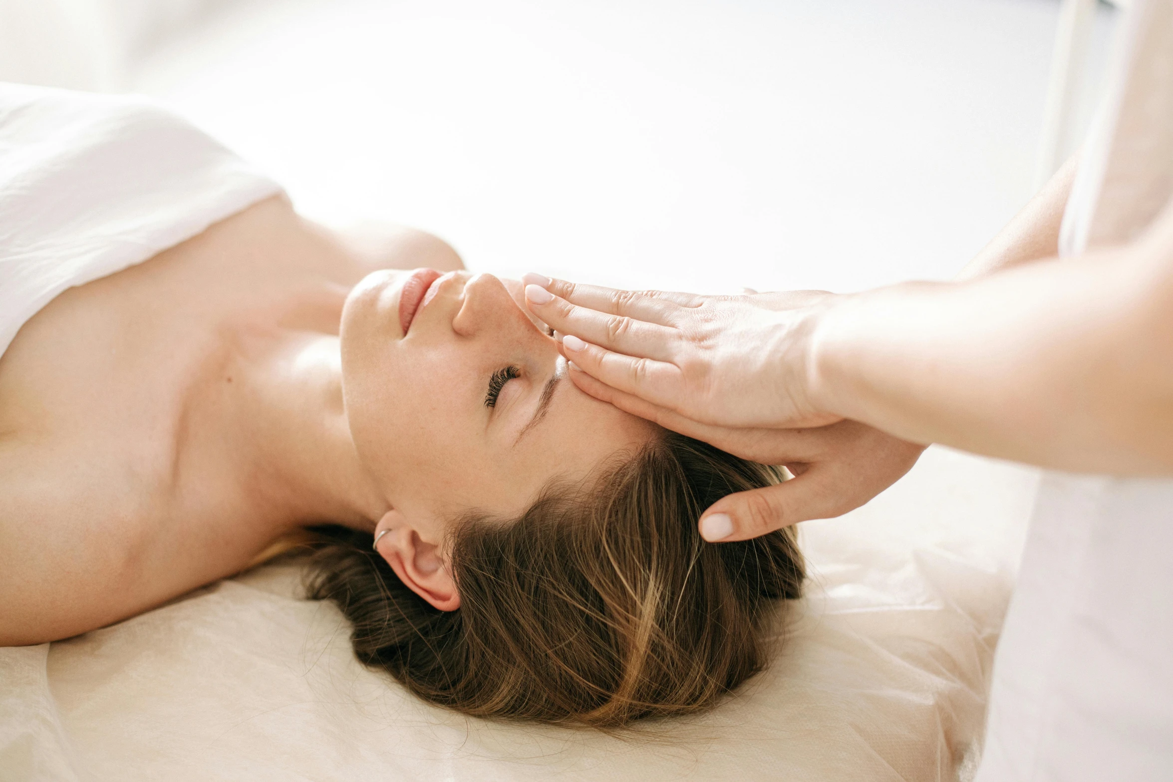 a woman laying on top of a bed while touching her forehead